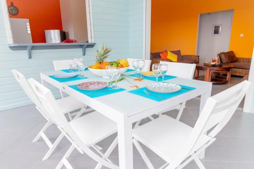 a white dining table and chairs with a bowl of fruit at Villa Arc-en-ciel in Le Moule