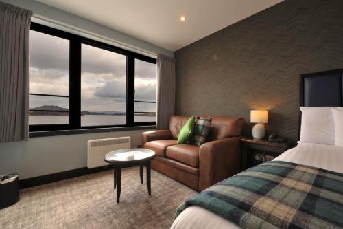 a hotel room with a bed and a couch and windows at The Lodge On Loch Lomond Hotel in Luss