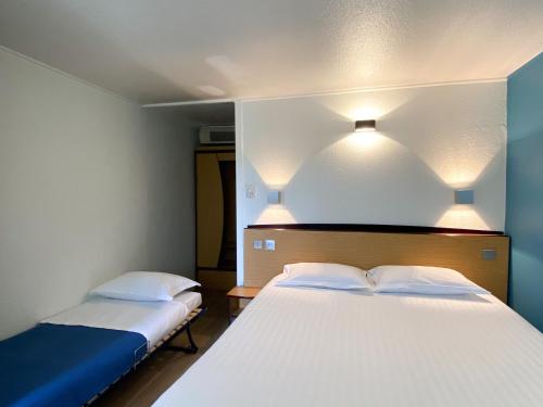 a bedroom with two beds with white sheets and lights at Kyriad Direct Roanne Hôtel in Roanne
