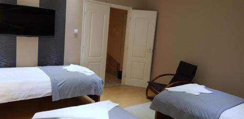 a room with two beds and a chair and a television at Alice Vendégház in Kalocsa
