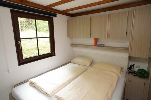 Bett in einem Zimmer mit Fenster in der Unterkunft Camping Harfenmühle - Chalet in Mörschied