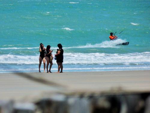 three people standing on a beach with a man in the ocean at Pousada Casa Azul do Piauí in Luis Correia