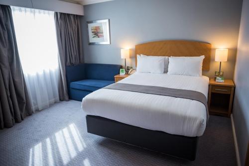 a hotel room with a bed and a blue chair at Holiday Inn Manchester West by IHG in Manchester