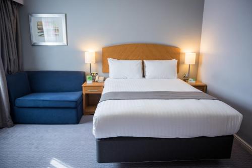 a hotel room with a bed and a blue chair at Holiday Inn Manchester West by IHG in Manchester