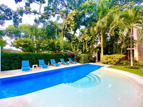 a swimming pool with blue chairs and palm trees at Villa Tendenza Condo in Playa del Carmen
