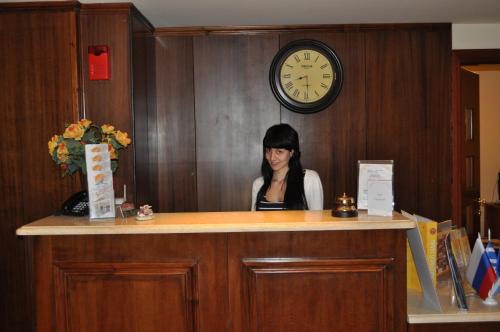 une femme assise au comptoir avec une horloge sur le mur dans l'établissement Corfu Secret Hotel, à Ýpsos