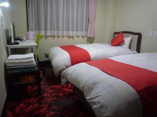 a bedroom with two beds with red and white sheets at Business Hotel Kyugetsu in Tsukumi