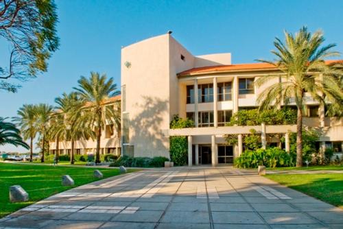 a large building with palm trees in front of it at Shefayim Kibbutz Hotel in Kibbutz Shefayim