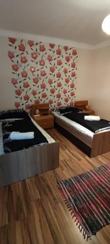 two beds in a room with a wall with flowers at Orsi Apartman / vendegház in Kecskemét