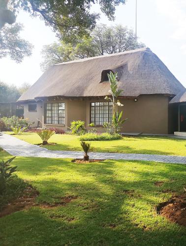 a house with a thatched roof and a grass yard at Sasavona Game Lodge in Warmbaths
