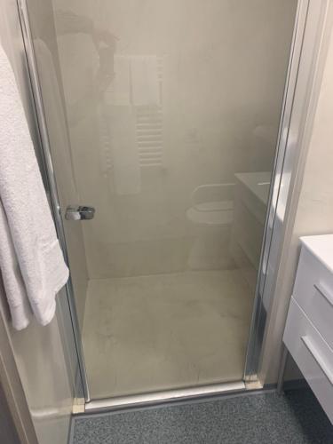 y baño con ducha y puerta de cristal. en Szelim Motel, en Tatabánya