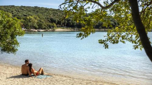 two people sitting on a beach near the water at PARADISE Beach Apartments in Rovinj