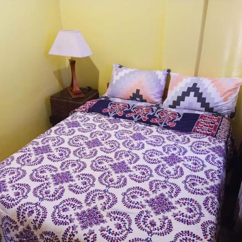 uma cama com um edredão roxo e branco e um candeeiro em Blue Nest Apartment em Manila