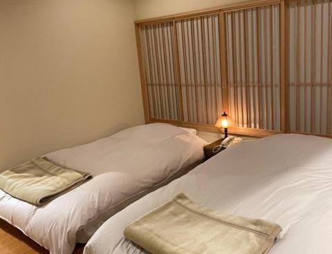 2 Betten in einem Zimmer mit einer Lampe daneben in der Unterkunft Ryokan Seifuso in Ōmuta