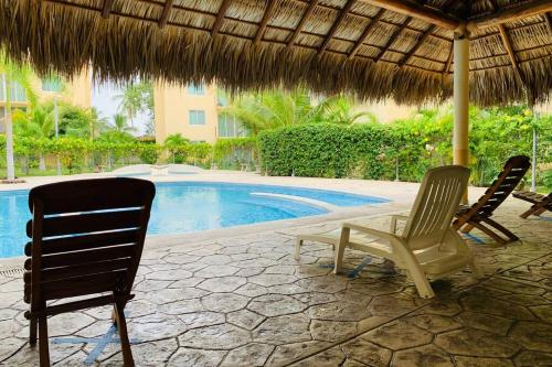 duas cadeiras e um guarda-sol junto a uma piscina em El Colorín, a condo in the heart of Huatulco em Santa Cruz, Huatulco