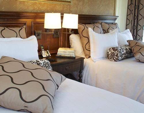 a bedroom with two beds and a table with two lamps at Norwalk Inn & Conference Center in Norwalk