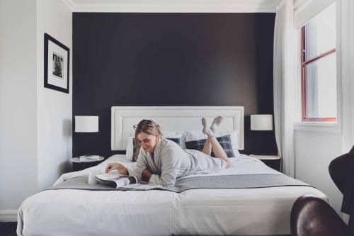 a woman laying on a bed reading a book at Perouse Randwick by Sydney Lodges in Sydney