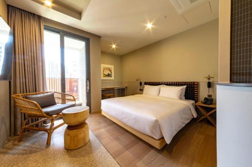 a bedroom with a bed and a chair and a window at Hound Garden&Terrace Hotel in Busan