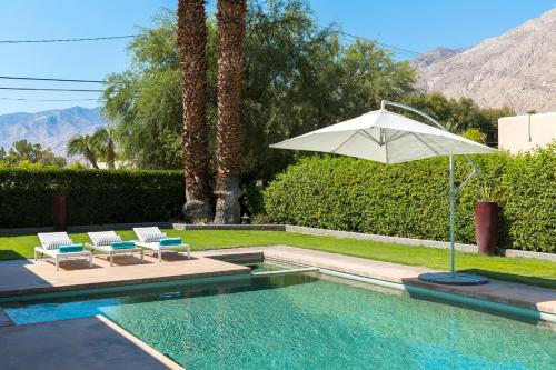 a swimming pool with an umbrella and two chairs at Villa Tranquilo home in Palm Springs