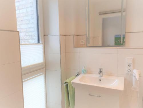 La salle de bains blanche est pourvue d'un lavabo et d'un miroir. dans l'établissement Apartment Jadestern, Am Alten Deich 4-6, 2 26, à Dangast