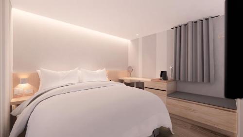 a white bedroom with a large bed and a desk at Ta Lee Hotel in Tainan