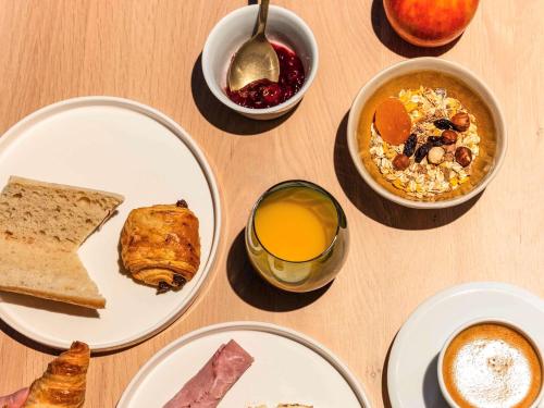 a table with plates of breakfast foods and a glass of orange juice at Mercure Saint Omer Centre Gare in Saint-Omer