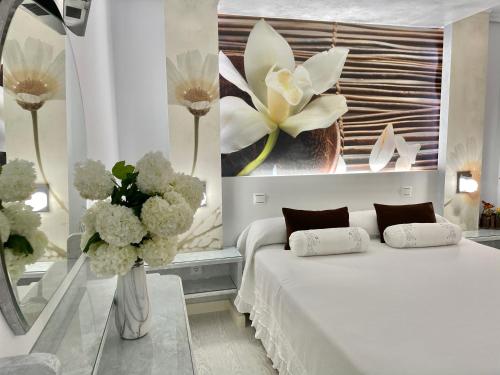 Un dormitorio con una cama blanca y un jarrón de flores en El Jardin en Soto de la Marina