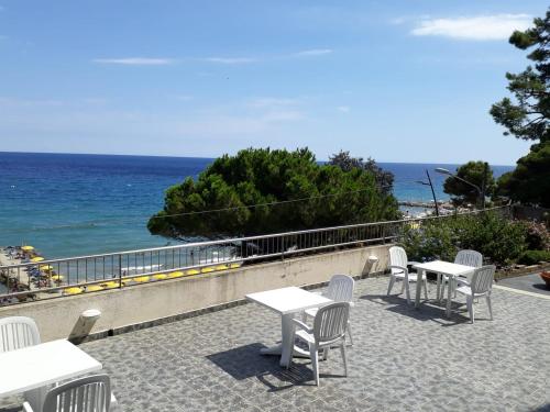 un patio con mesas y sillas blancas y el océano en Residence Paradiso en Laigueglia