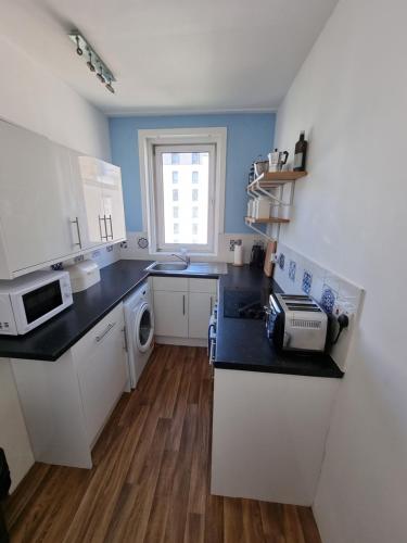 a kitchen with white cabinets and a black counter top at Bespoke Tours Scotland Accommodation @ Morrison Street in Edinburgh