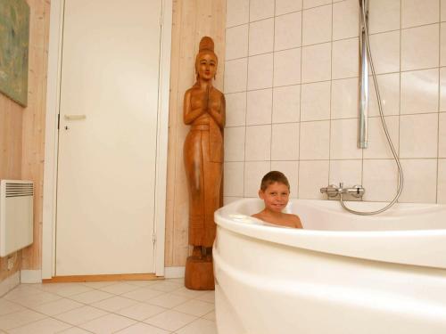 a boy sitting in a bath tub next to a statue at 6 person holiday home in Dronningm lle in Gilleleje