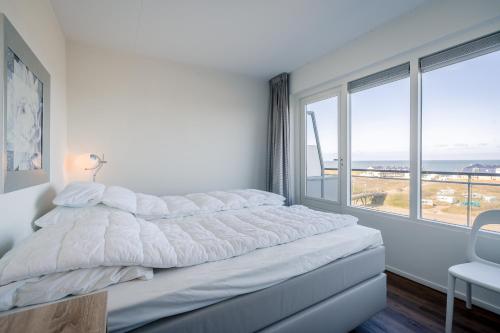 ein weißes Schlafzimmer mit einem Bett und einem großen Fenster in der Unterkunft Appartementencomplex Juliana 154 in De Koog