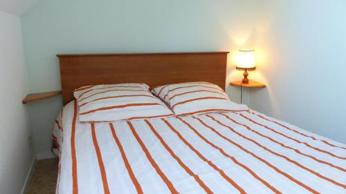 a bed with striped sheets and a lamp next to it at Erdeven - Petite maison de vacances près de la plage de Kerhilio in Erdeven