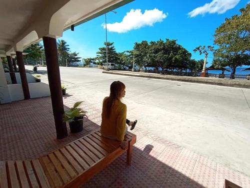 a woman sitting on a bench next to a street at La Frezza Beach House in Bayawan