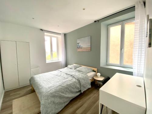 Un dormitorio con una cama y una mesa y dos ventanas. en Très beau T2 42m2 lumineux, moderne et rénové avec Fibre, en Belfort