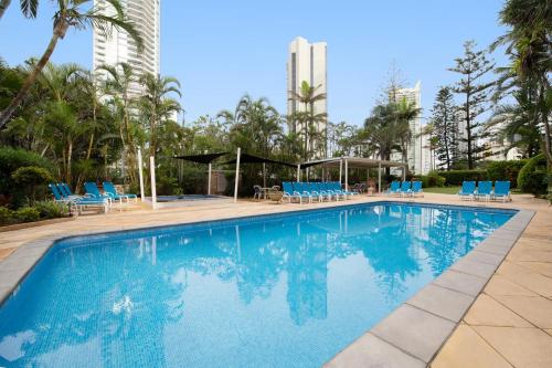 a large swimming pool with blue chairs and palm trees at BreakFree Beachpoint in Gold Coast