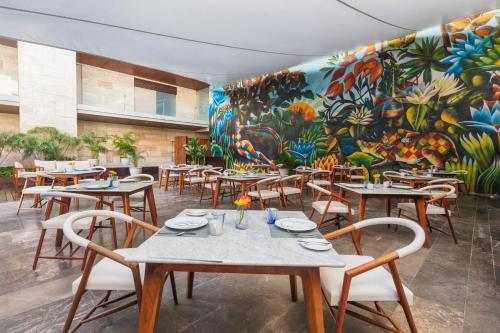 a restaurant with tables and chairs and a mural at The Yucatan Playa Del Carmen, Tapestry Collection By Hilton in Playa del Carmen