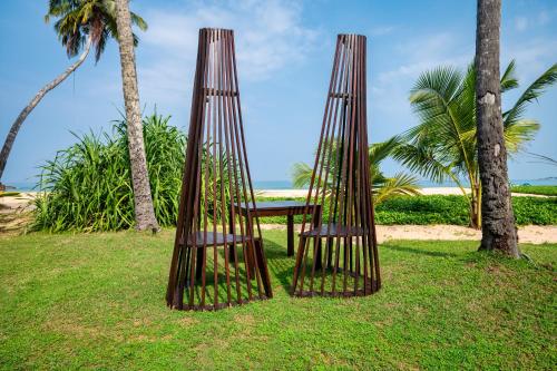 two wooden chairs sitting in the grass next to palm trees at Shinagawa Beach in Balapitiya