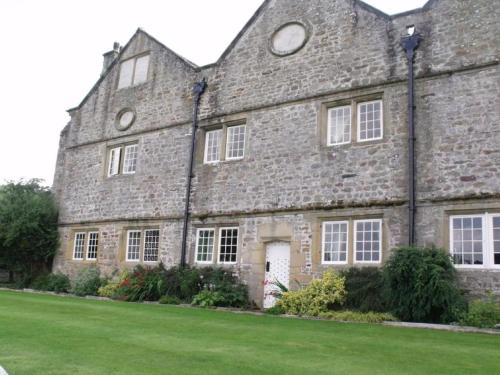 un gran edificio de piedra con un césped verde delante de él en Braithwaite Hall Apartment, en East Witton