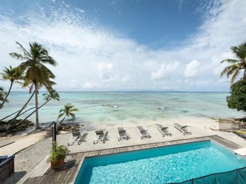 a swimming pool next to a beach with chairs and the ocean at Coco Beach Marie-Galante in Grand-Bourg