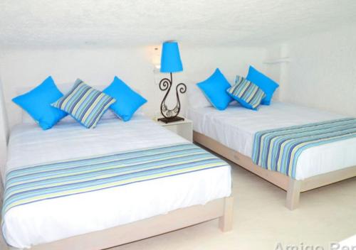 two beds in a white room with blue pillows at Apartamento Frente a la Playa Cancun Mexico in Cancún