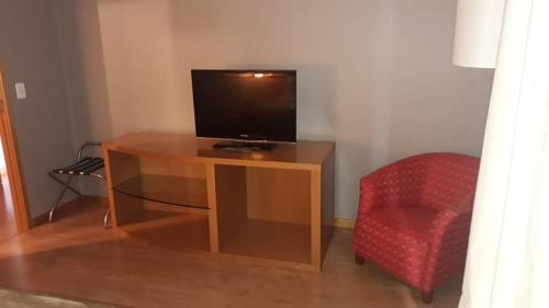 einen Holzschreibtisch mit einem TV und einem roten Stuhl in der Unterkunft Apartamento no condomínio do Brasil 21 Suites in Brasilia