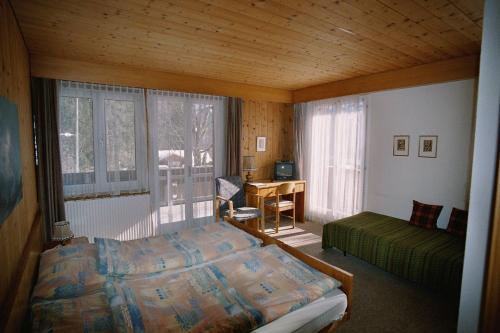 a bedroom with a bed and a desk and windows at Hotel Bellary in Grindelwald