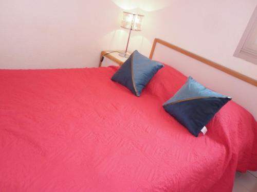 - un lit rouge avec 2 oreillers bleus dans l'établissement Appartement 2 Pièces Vue Piscine plage Richelieu CAP D'AGDE, au Cap d'Agde
