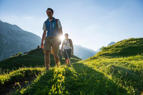 a man and woman walking on a grassy hill with the sun behind them at Alpine Lodge Klösterle am Arlberg in Klösterle am Arlberg