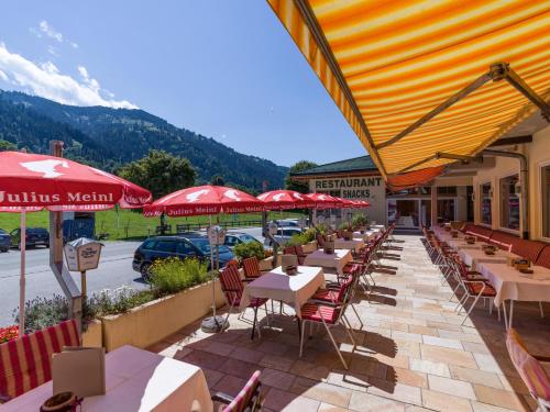 a row of tables and chairs with red umbrellas on a patio at Harmony Hotel Harfenwirt in Niederau
