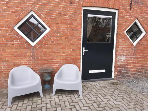twee witte stoelen voor een bakstenen gebouw met een deur bij Appartementen Hoek 2 in Baflo