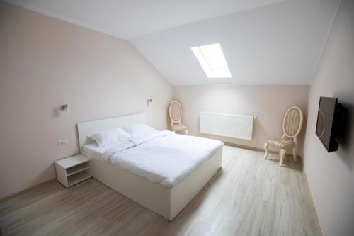 a white bedroom with a bed and two chairs at Regal Ballroom in Caransebeş