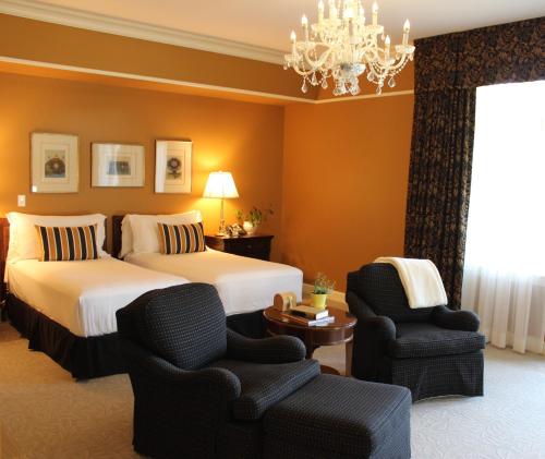 a hotel room with two beds and chairs and a chandelier at The Bruce Hotel in Stratford