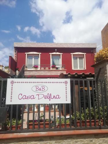 een rood huis met een bord op een hek bij B&B Casa Delfina in Capoterra