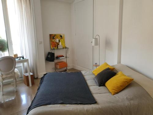 Appartement Centre ville carré d'Or في مونت كارلو: غرفة نوم مع سرير مع وسائد صفراء ومكتب